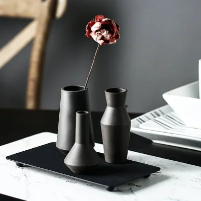 Three black ceramic vases on a black metal tray with one red dried flower