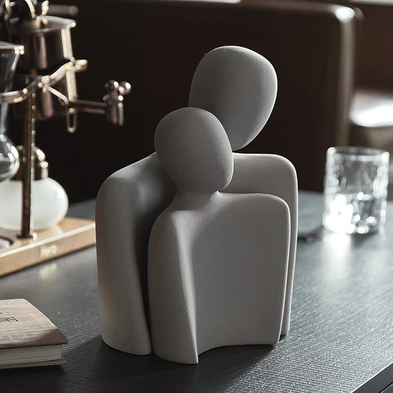 Two light abstract figure sculptures on a dark wood table