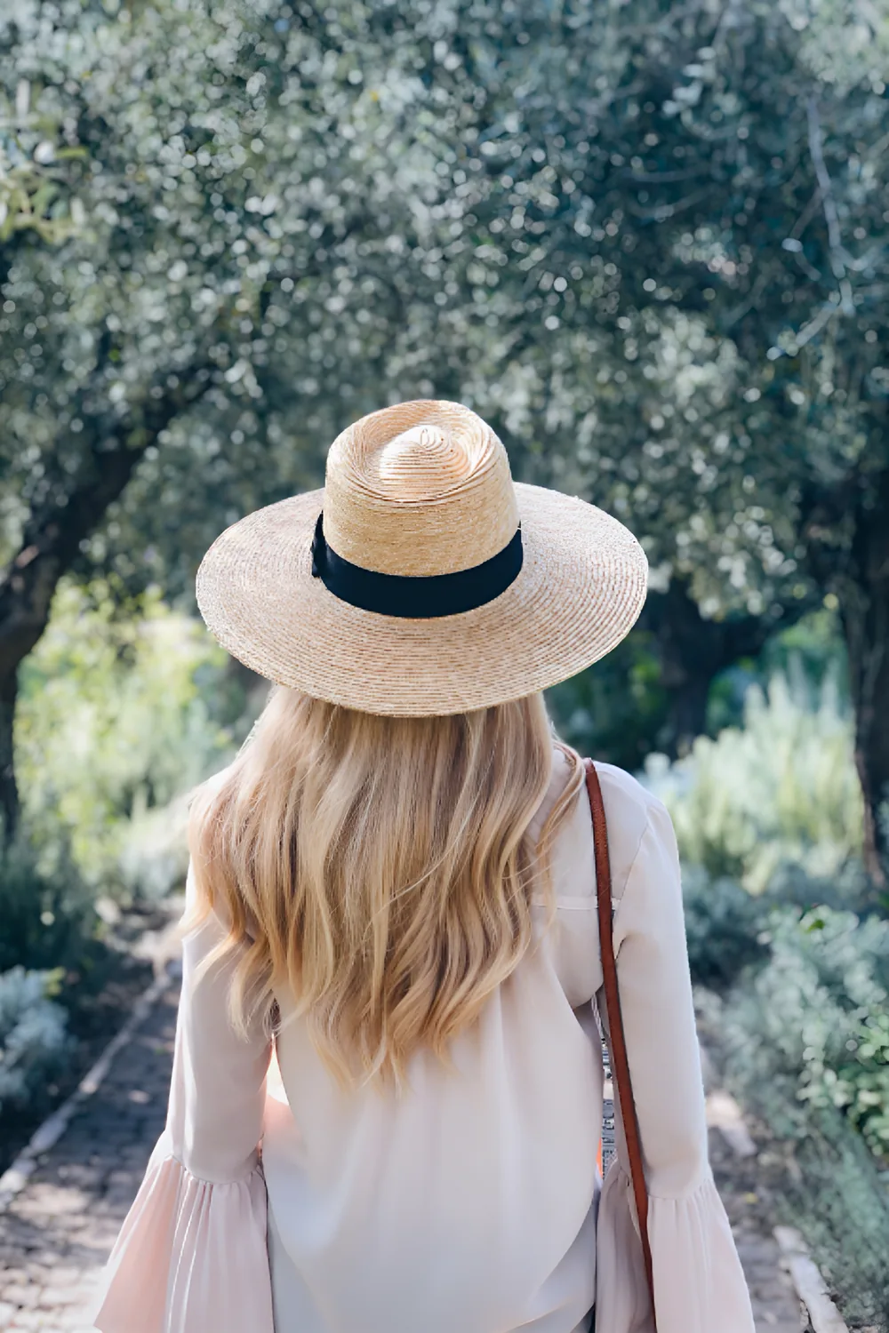 Woman in a straw sun hat walking down a garden path, seen from behind