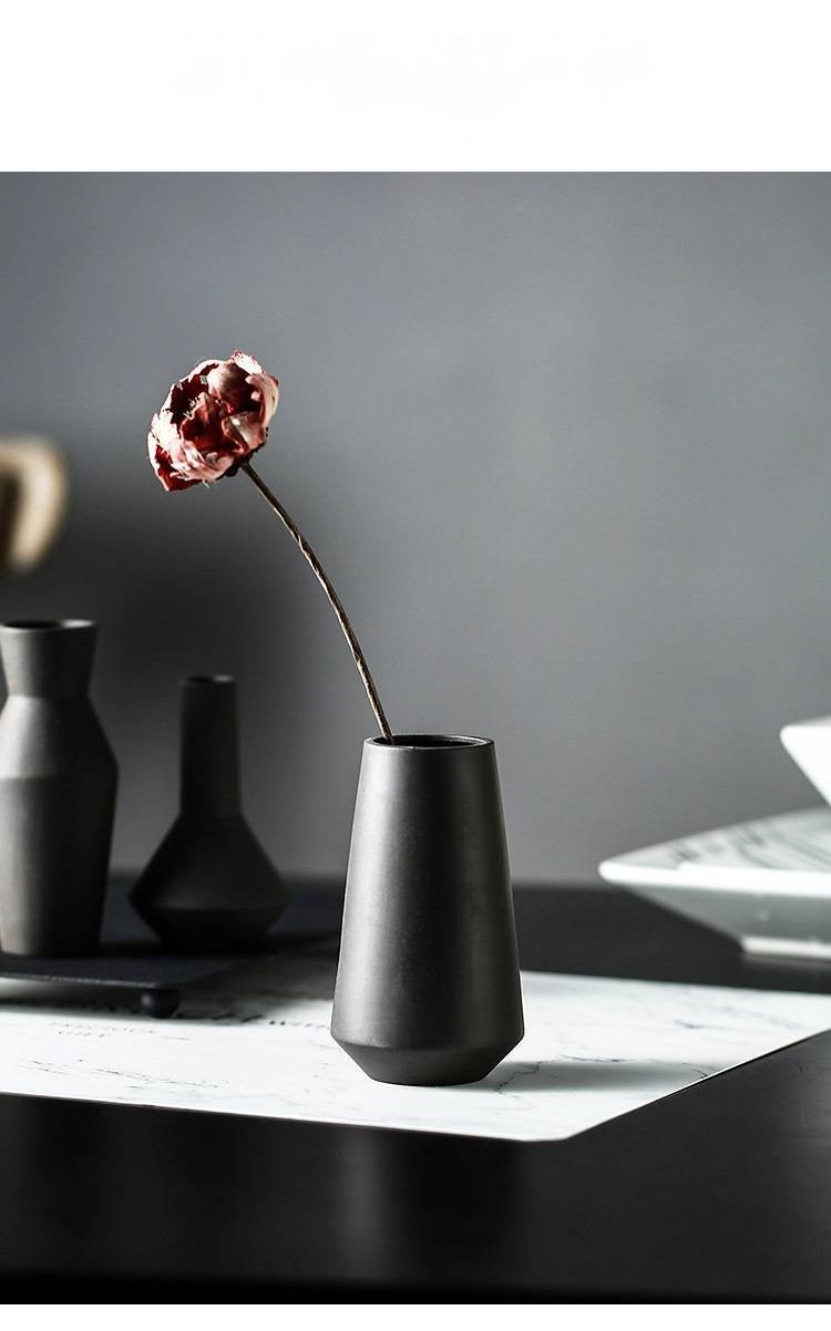 Black ceramic vase holding one dried flower on a dining table
