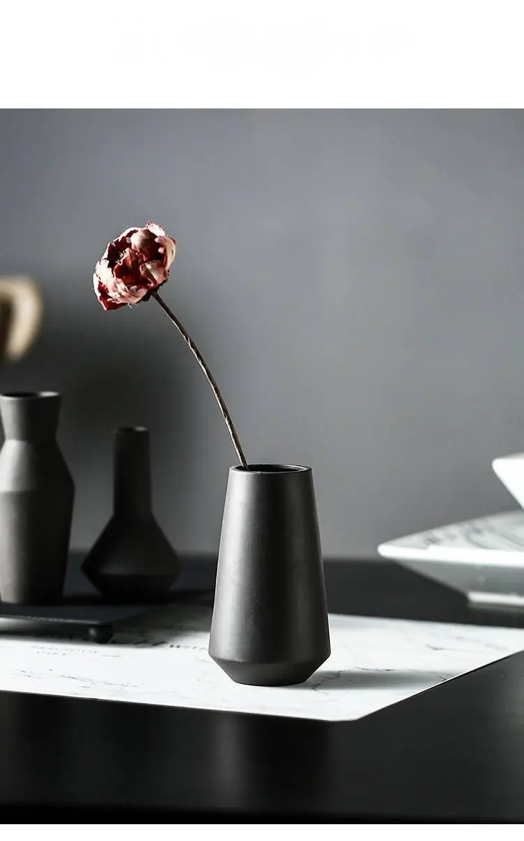 Black ceramic vase holding one dried flower on a dining table